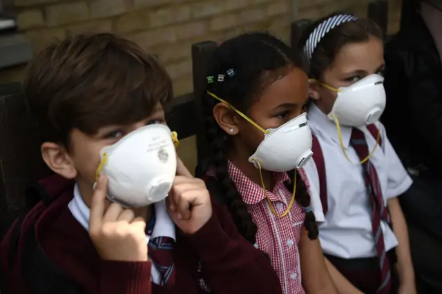 Young children attending school near the site of the Grenfell Tower fire wear protective face masks