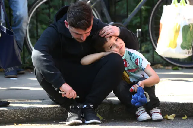 A man comforts a child near Grenfell Tower