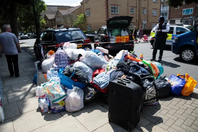 A pile of donated clothes, sleeping bags and water lie next to a police cordon near the burning the 24 storey residential Grenfell Tower block in Latimer Road, West London