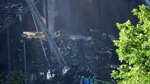 Firefighters use a riot shield as protection from falling rubble