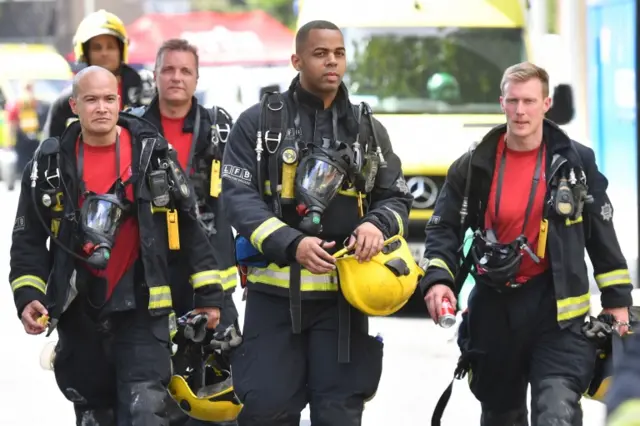 Five firefighters walk together at the scene where a fire ripped through Grenfell Tower on June 14, 2017.