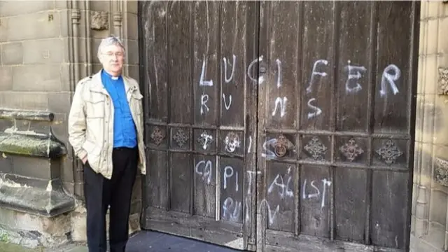 Rev Alan Gordon stands next to the graffiti