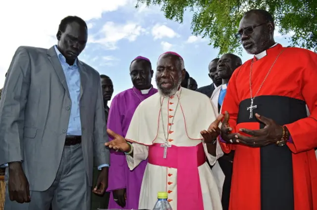 South Sudan rebel leader of the Democratic Movement/Army (SSDM/A) faction David Yau Yau (L) stands with Bishop Paride Taban (C) who was a mediator in the Jonglei peace process during a prayer in Gumuruk on May 13, 2014.