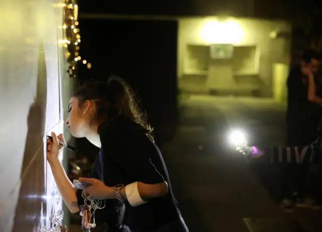 Woman writing a message of condolence on a wall