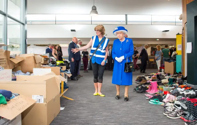 Queen Elizabeth II is shown donations of aid made by members of the local community by Executive Director of Kensington and Chelsea Council Sue Harris during a visit to the Westway Sports Centre, London