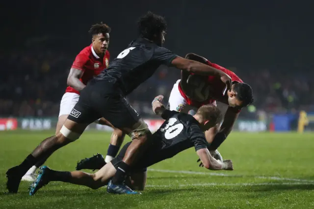 Ben Te"o of the Lions is hauled down short of the tryline by Akira Ioane and Damian McKenzie of the Maori All Blacks