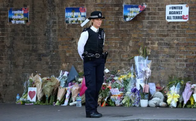 A police officer stands on duty near tributes and flowers at a police cordon in Finsbury Park area of north London on June 19, 2017, following a vehicle attack on pedestrians