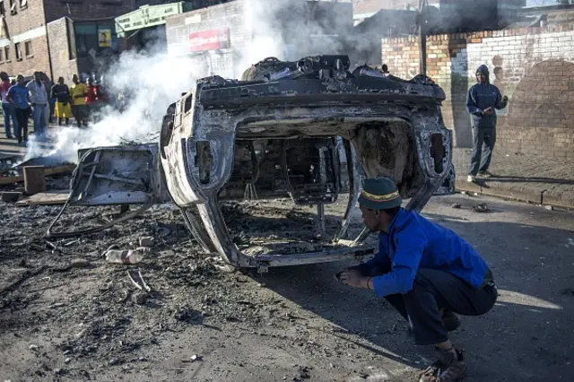 People look at a burnt-out car purportedly torched in the early hours outside the Jeppies Hostles, in the Jeppestown area of Johannesburg, on April 17, 2015.