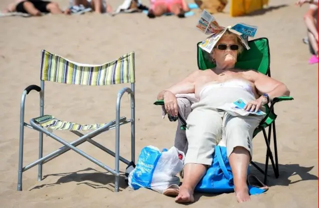 Eldery woman sitting in a deckchair on a beach, with newspaper covering her head