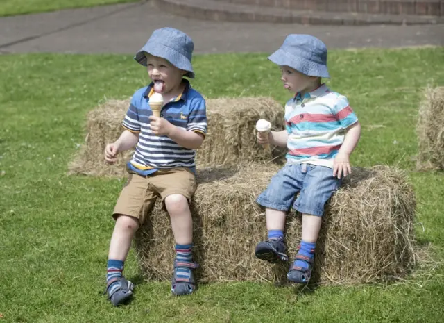 Two young boys sit on a hay bale, with ice creams