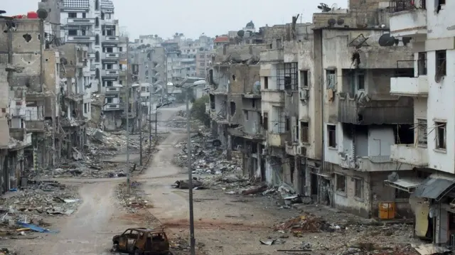 A man walks past damaged buildings along a street at the Khalidiya district of Homs, Syria (19 November 2012)