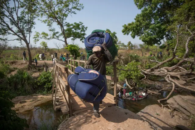 South Sudanese refugees cross a small wooden bridge over a river from South Sudan into Uganda on February 24, 2017