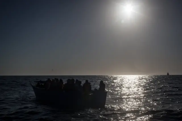 Migrants wait in a small wooden boat