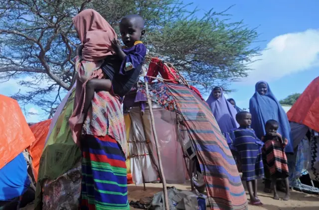 A displaced Somali woman carries her child on her back on May 24, 2017 at a makeshift camp in the Garasbaley area on the outskirts of the capital Mogadishu, where people converge after fleeing their homes due to the dire drought that hits the country.