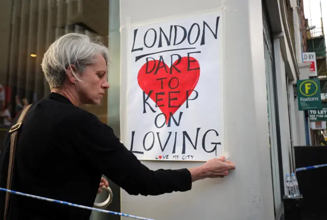 A woman places a sign saying, "London, dare to keep on loving"