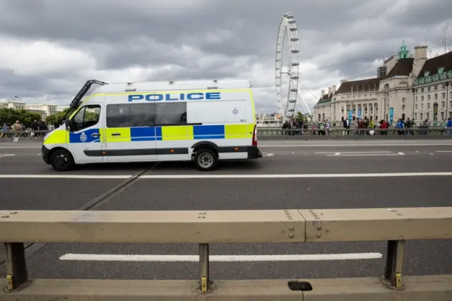 A police van drives past a security barrier between the road and pavement of Westminster Bridge