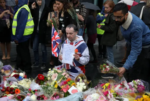 A man kneels in front of flowers left near City Hall