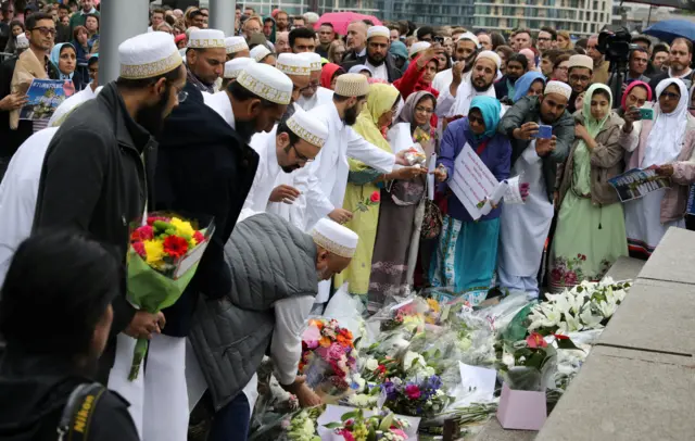 Men dressed in traditional robes lay flowers at a memorial near Tower Bridge