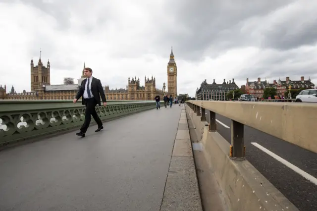 A man walks past a security barrier which sits between the road and pavement of Westminster Bridge in London