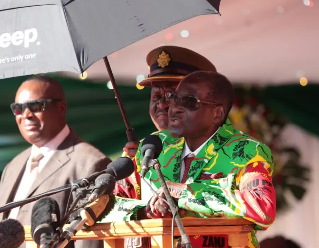 Zimbabwean President Robert Mugabe (R) is shaded with an umbrella as he addresses a gathering of youth at the Rudhaka Stadium in Marondera, about 100 kilometers east of Harare, Zimbabwe, 02 June 2017.