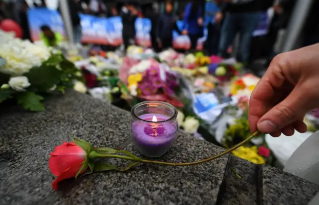 Someone lays a rose next to a candle outside City Hall