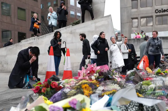 A man kneels and covers his eyes as he kneels beside flowers south of London Bridge in London