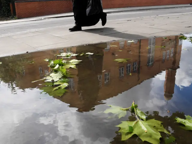 A man walks past a puddle reflecting the Al Madina Mosque in Barking, Britain