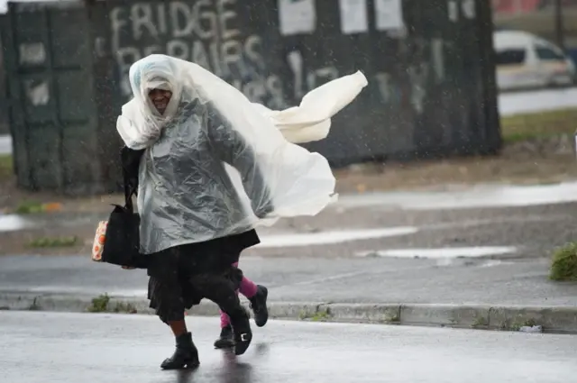 A woman and a child run across the road, in makeshift raincoats in an informal settlement, in Langa, during one of the most intense storms that has hit the Western Cape Province in more than a decade, on June 07, 2016, in Cape Town