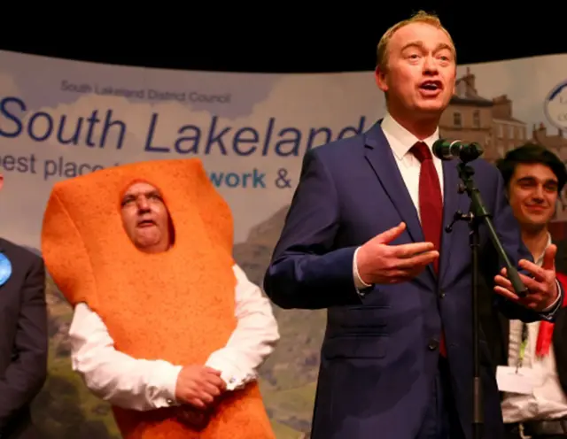 Lib Dem leader speaks, while opponent Mr Fishfinger gurns in the background