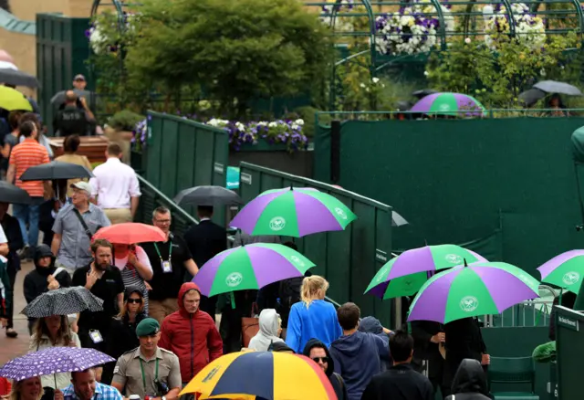 Spectators shelter under umbrellas as rain falls on day eight of the Wimbledon Championships