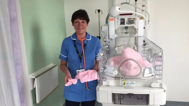 A nurse holding a knitted cardigan and booties for a baby