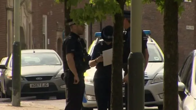 Police officers standing in street alongside police vehicles