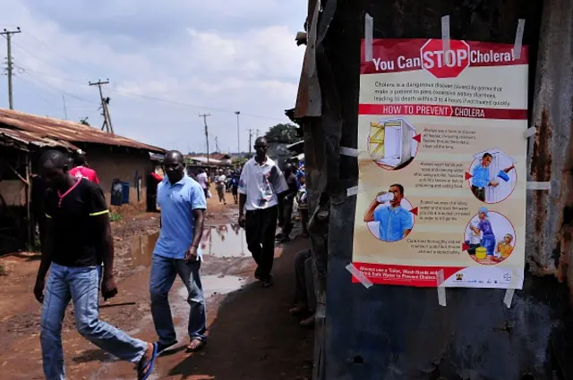 People walk past a kiosk where a poster giving information on how to prevent Cholera is displayed in the Kibera area of Nairobi on May 20, 2015