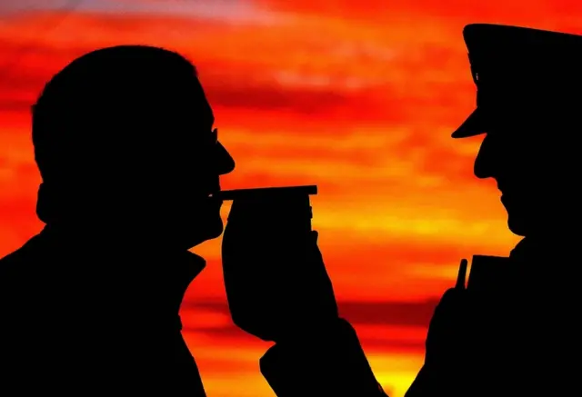 Silhouette shows a motorist stopped by police giving a breath test on a breathalyser