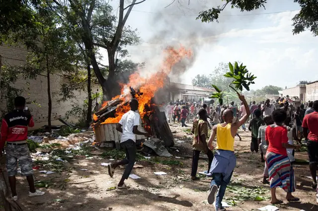 A man holding up a branch runs past a fire burning as people loot a local police station in the the Buyenzi neighborhood of Bujumbura on May 13, 2015