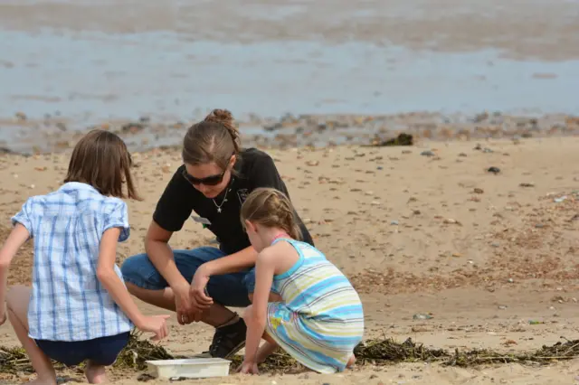 Two young girls and an adult searching the sandline