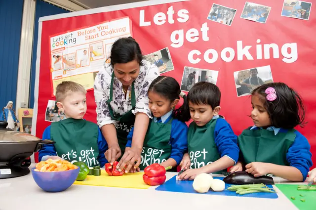 Woman showing four children how to chop peppers