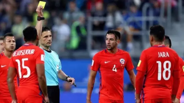 Referee Milorad Mazic booking Chile's Gonzalo Jara