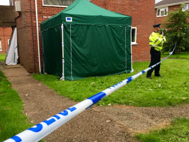 Police tape, and police officer stand by forensic tent outside the property