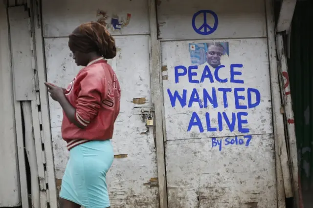 A woman walks past a shop with a message of peace painted recently by local street artist Solomon Muyundo, also known as Solo7, on its door in Kibera slum, one of the opposition leader Raila Odinga"s strongholds in the capital Nairobi, Kenya, 23 July 2017