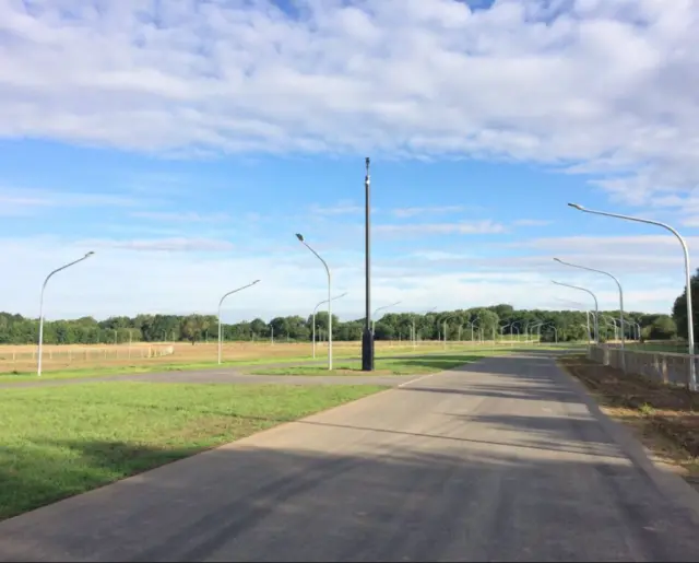 Wide Cycle track surrounded by grass and street lights and fields.