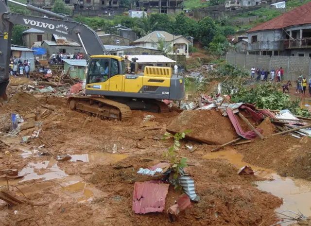 A digger clears debris from damage to property caused by a mudslide in the suburb of Regent behind Guma reservoir, Freetown, Sierra Leone