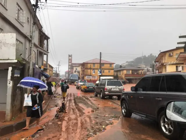 People walk under rain along a street in Freetown, Sierra Leone August 14, 2017 in this picture obtained from social media.