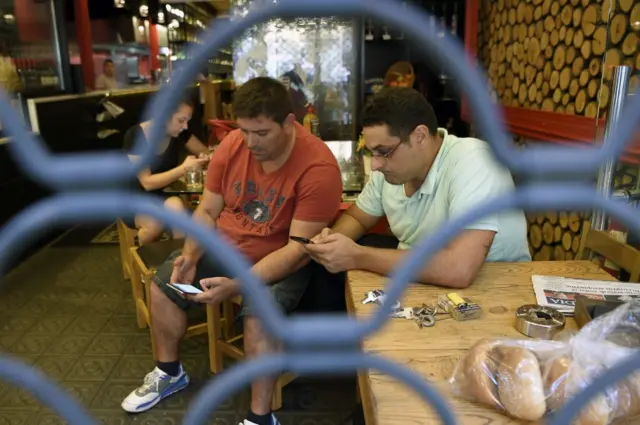 People check their smartphones in a bar behind an iron curtain as they wait after a van ploughed into the crowd