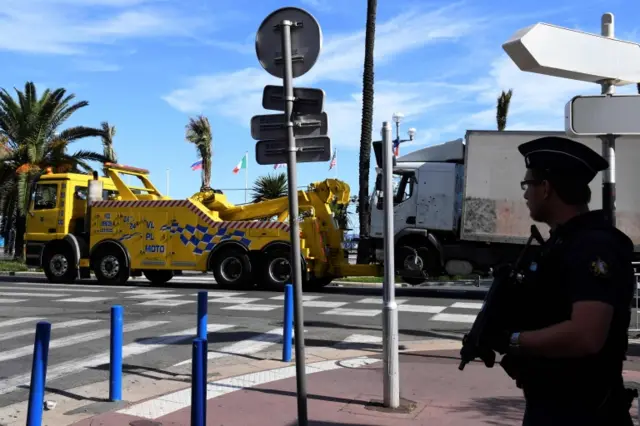 a police officer standing guard as the truck that was driven by a man through a crowd celebrating Bastille Day is towed away by a breakdown lorry in the French Riviera city of Nice.