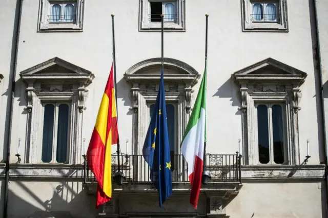 Italian, Spanish and European Union flags are flown at a half-mast at the entry of the Chigi Palace in Rome, Italy.