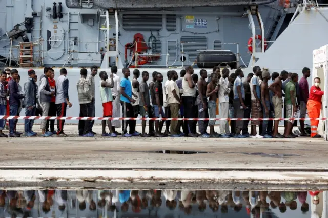 Migrants stand in line after disembarking from the Italian Navy vessel Bersagliare at the Sicilian port of Augusta