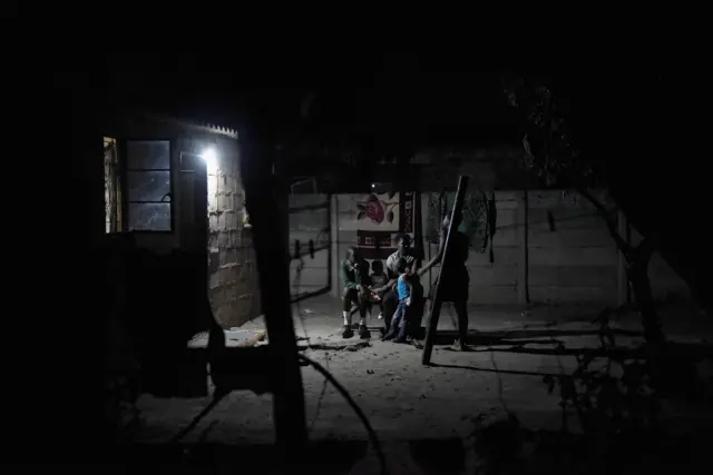 A family sit outside and share food by torchlight, after darkness falls in the Harare suburb of Chitungwiza where electricity is only provided for a few hours, usually after around 9pm, Chitungwiza, Zimbabwe on October 8th 2015