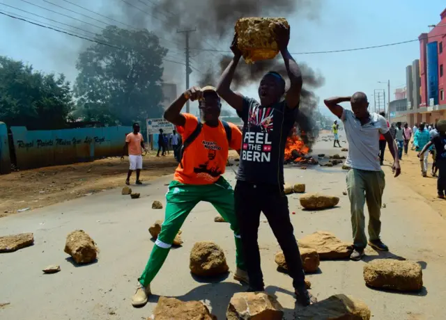 enyan National Super Alliance (NASA) supporters hold rocks as they stand in front of a burning barricade on a road in Kisumu on August 9, 2017, as they clash with security personnel after the announcement of national election results.