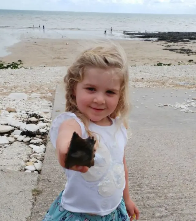 A little girl holding a Small-eyed Ray egg case.